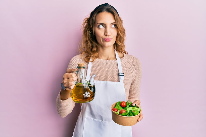 Frau hält Kanne mit Öl und einen Salat in den Händen
