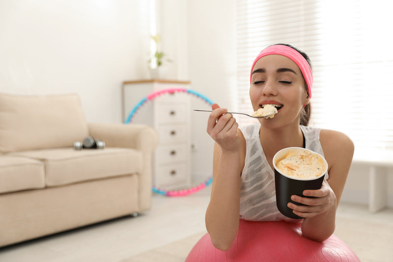 Protein Eis: Frau in Sportkleidung isst Eis aus einem Becher