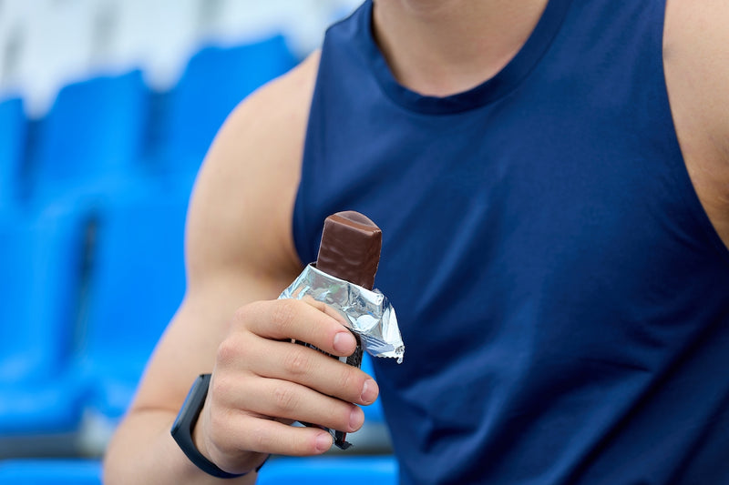 Gute Eiweißriegel: Mann im Sportoutfit hält Proteinriegel in der Hand
