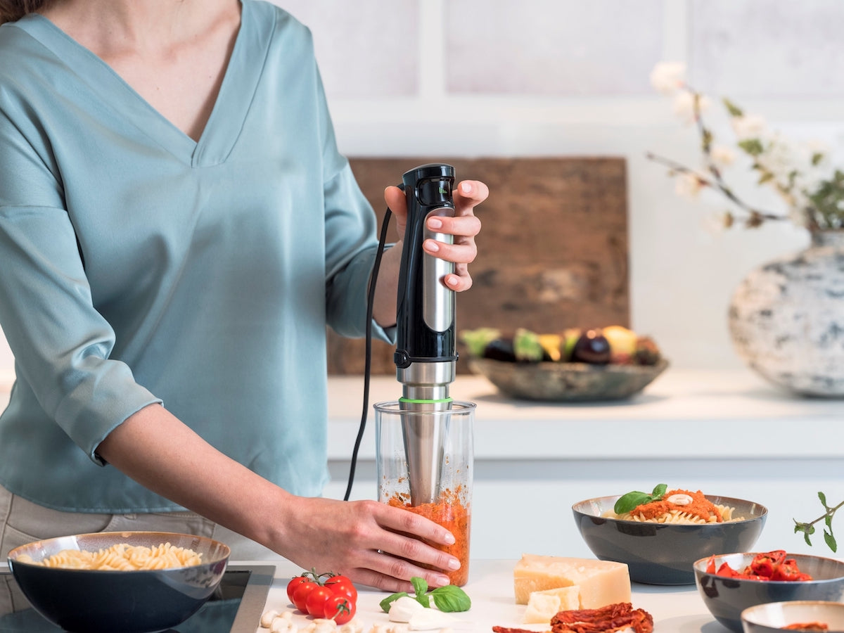 Frau zerkleinert Essen mit dem Pürierstab