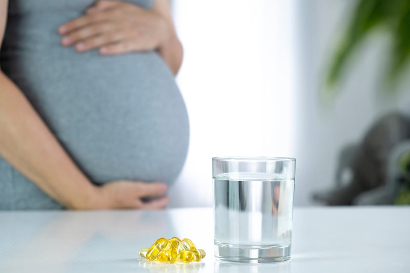 Nährstoffe in der Schwangerschaft: Schwangere Frau und davor Glas Wasser und Nahrungsergänzungsmittel auf einem Tisch