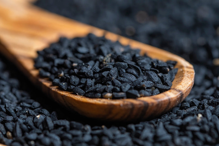 Schwarzkümmelöl Wirkung: Schwarze Samen des Schwarzkümmels auf einem Holzlöffel