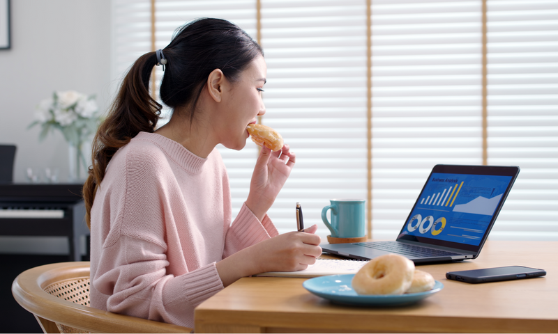 Frau isst Donuts vor dem Laptop