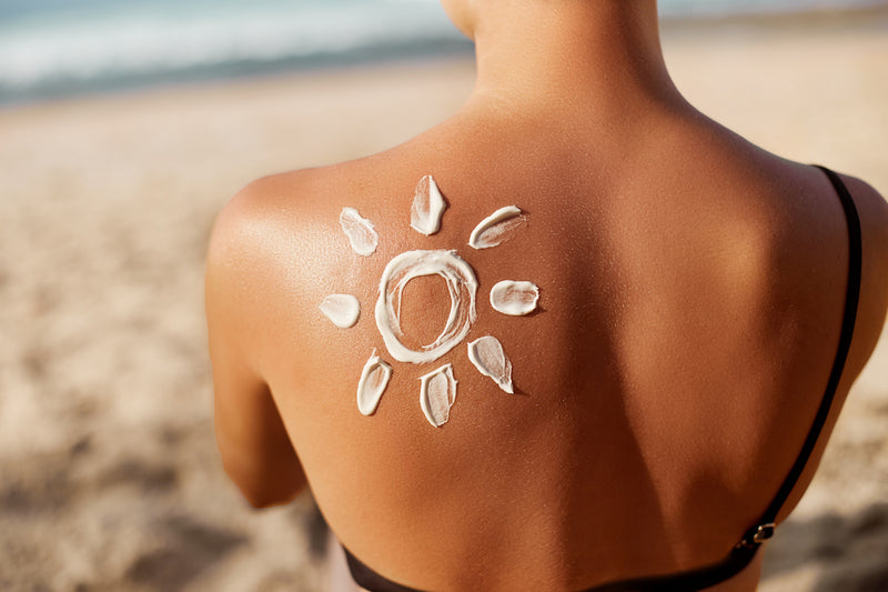 Tipps gegen Hitze: Frau am Strand hat eine Sonne aus Sonnencreme auf dem Rücken